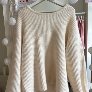 Krämvit stickad tröja med rosett Gina Tricot - Superfin krämvit stickad tröja från Gina Tricot med ribbad struktur och stor rosett i ryggen. Tröjan har lång ärm, öppen rygg.