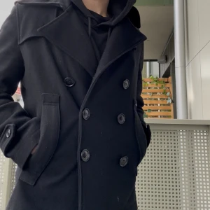 Svart skepparkavaj/peacoat  - Säljer en svart skepparkavaj/peacoat med dubbelknäppning. Jackan har klassiska knappar framtill och på ärmsluten, samt två fickor med lock. Perfekt för dig som vill ha en stilren och tidlös look under höst och vinter.
