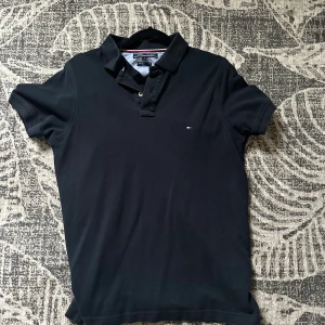 Svart pikétröja Tommy Hilfiger  - Klassisk svart pikétröja från Tommy Hilfiger i storlek S. Tröjan har korta ärmar, krage med knappar och den ikoniska lilla loggan broderad på bröstet. Tillverkad i bomull för en skön och stilren känsla. Knappt använd så skicket är 9/10. Kontakta mig vid frågor eller pris.