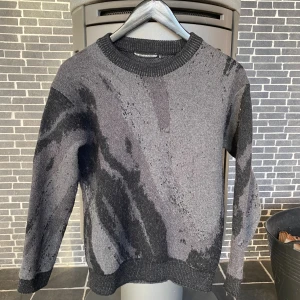 Grå och svart stickad tröja Issey Miyake - Säljer en unik stickad tröja från Issey Miyake Men i grått och svart med abstrakt mönster. Tröjan har rund halsringning, ribbade muddar och är tillverkad i en mjuk ull- och bomullsblandning. . Köptes för 2300 på etresex på Södermalm 