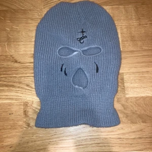 Grå stickad balaclava - Säljer en nästan oanvänd grå stickad balaclava. Masken har tre hål för ögon och mun, och är stickad för extra komfort och stil. Perfekt för kalla dagar eller när du vill sticka ut.