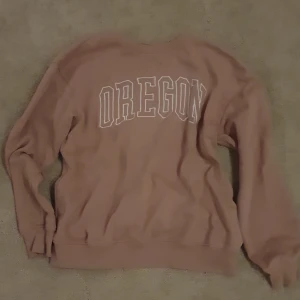 Rosa sweatshirt Oregon från 157 - Säljer en oversized rosa sweatshirt från 157 med stort vitt OREGON-tryck på bröstet. Tröjan har rund hals, långa ärmar och mjukt material som känns skönt mot huden. Perfekt för chill dagar och enkel att matcha med jeans eller kjol.