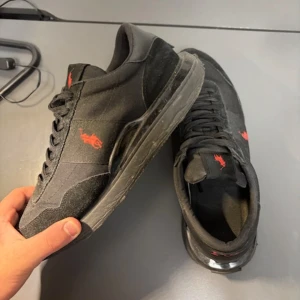Svarta Polo Ralph Lauren sneakers - Svarta sneakers från Polo Ralph Lauren med röd logga på sidan och hälen. Skorna tvättas innan dom skickas så dom blir som nya. Storlek 41 och jag säljer dom för endast 699kr