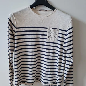 Randig långärmad tröja från Lindex strl 170 (barn) - Säljer en vit och marinblå långärmad tröja från Lindex Kids i 100% bomull. Tröjan har klassiskt randigt mönster och en liten bröstficka med tryck.   Storlek 170.  Kan hämtas i Vallentuna.