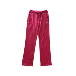 Rosa velourbyxor Juicy Couture S - Rosa mjukisbyxor från Juicy Couture i glansig velour med snörning i midjan och raka ben. På baksidan står det 'Juicy' i glittriga stenar. Klassisk logga framtill och bekväm passform, perfekta för en chill look.