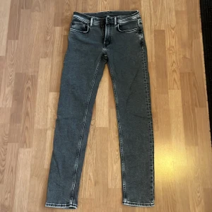 Grå jeans från Acne Studios - Snygga grå jeans från Acne Studios med slim passform. Jeansen har en mörkgrå tvätt med ljusare slitningar och detaljerade sömmar. Tillverkade i jeanstyg med skön stretch och har läderpatch med logga bak i midjan.                              Ytterbenslängd: 107cm Innerbenslängd: 79cm                         Midja: 40cm                                                                                 Tveka inte på att skriva ifall du undrar nåt!✨  