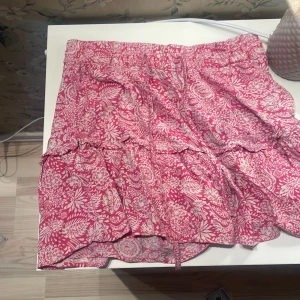 Rosa blommig kortkjol från Zara - Supersöt kortkjol från Zara i rosa och vitt med blommigt mönster. Kjolen har volangdetaljer och resår i midjan för en bekväm passform. Perfekt för dig som gillar en feminin och somrig stil.