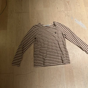 Randig långärmad tröja Carin Wester - Säljer en beige och brun långärmad tröja från Carin Wester med smala horisontella ränder och broderad logga på bröstet. Tröjan har rund hals och är gjord i mjuk bomull, perfekt för chill dagar. Passar dig som gillar enkel och clean stil.