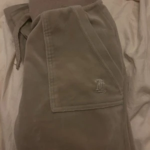 Beige mjukisbyxor Juicy Couture XXS men passar även Xs  - Supermjuka beige mjukisbyxor från Juicy Couture med broderad JC-logga framtill och två bakfickor med silvriga knappar. Byxorna har bred resår i midjan och är perfekta för en chill och avslappnad stil.