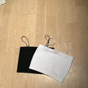 Svart och vit bandeau tubtopp - Två stilrena bandeau tubtoppar i svart och vit med smala axelband. Perfekt för att skapa en clean och enkel look. Materialet känns mjukt och stretchigt, vilket gör dem sköna att bära. Snygga att matcha med jeans eller kjol för en trendig vibe. Båda kommer med köpet!