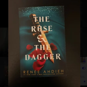 The Rose & The Dagger - En spännande bok med ett mystiskt omslag som visar en dolk och rosenblad mot en blå bakgrund. Perfekt för dig som gillar dramatiska berättelser och episka äventyr. Skriven av Renée Ahdieh, en bästsäljande författare.