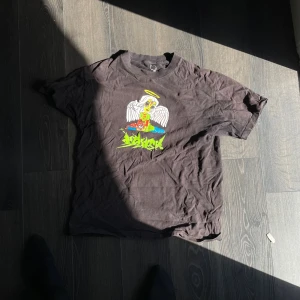 Svart t-shirt med grafiskt tryck WKND - Svart t-shirt från WKND i 100% bomull med färgglatt grafiskt tryck på bröstet som föreställer en tecknad ängel med vingar och halo. Klassisk passform och rund halsringning. Perfekt för dig som gillar streetwear vibes.