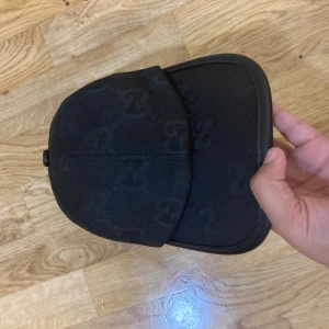 Svart keps - Säljer en svart keps  med diskret över hela kepsen. Kepsen har en bred, rundad skärm och justerbar rem baktill i skinn. Materialet är slitstark bomull och skinn, perfekt för dig som gillar exklusiva streetwear-vibes.