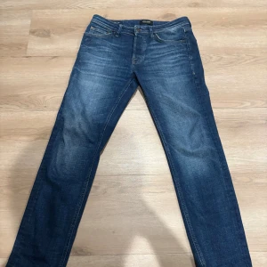 Blå tapered jeans från Jack & Jones - Snygga blå jeans från Jack & Jones i modellen Tapered/Mike. Jeansen har klassisk femficksdesign, normal midja och avsmalnande ben. Tillverkade i slitstarkt denim med snygga slitningar och kontrastsömmar. Perfekta för en avslappnad och trendig look. L - 32