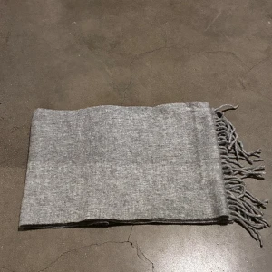 Grå halsduk från Tiger of Sweden - Stilren grå halsduk från Tiger of Sweden med klassiska fransar i ändarna. Tillverkad i en lyxig blandning av 90% ull och 10% kashmir som gör den både mjuk och varm. Perfekt accessoar för att lyfta din outfit under kyliga dagar. Deras pris 1000kr mitt pris 599. Den är relativ nu inga defekter