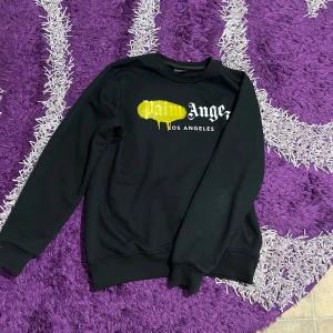 Svart Palm Angels sweatshirt S - Svart sweatshirt från Palm Angels i storlek S med ikonisk logga och gul drip-effekt på bröstet. Tröjan har rund hals, ribbade muddar och är långärmad. Materialet är mjukt och känns som bomull eller polyester. Perfekt för dig som gillar streetwear och vill sticka ut.