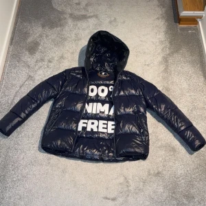 Mörkblå Save The Duck jacka - Snygg mörkblå pufferjacka från Save The Duck med glansig finish och huva. Jackan har dragkedja framtill och två sidofickor med dragkedja. Perfekt för kalla dagar och har en modern, ungdomlig look. Använd några gånger och ser nästan ny ut. Köpt från själva Save The Duck hemsidan.