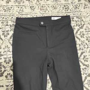 Svarta kostymbyxor från Zara - Snygga svarta kostymbyxor från Zara med raka ben och diskreta fickor framtill. Byxorna har en klassisk midja och stängs med knapp och dragkedja. Perfekta för en clean och stilren look.