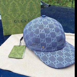 Blå Gucci keps - Säljer en blå keps från Gucci med ikoniskt GG-monogram i ljusare blått över hela kepsen. Kepsen har böjd skärm, justerbar rem bak och en liten guldfärgad GG-detalj på sidan. Tillverkad i bomullscanvas och levereras med originalförpackning och tags.