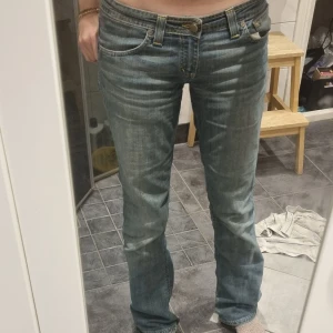 Blå bootcut jeans från Denimbirds - Säljer ett par superlågmidjade blå bootcut jeans från Denimbirds i storlek 31/34. De har inga tecken på användning och passar perfekt på mig som är 172 cm.Jeansen har klassisk femficksdesign, snygga slitningar och kontrastsömmar i gult. Modellen har låg midja och är tillverkad i mjukt denimtyg som sitter skönt hela dagen.
