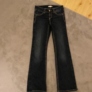 Mörkblå bootcut jeans Gina Tricot - Pris kan diskuteras Mörkblå jeans från Gina Tricot med bootcut passform och kontrastsömmar. Snygg broderad bakficka med paljettdetaljer som ger extra edge. Klassisk femficksmodell och knappstängning framtill. Perfekta för dig som gillar en cool och unik look.