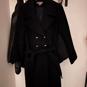 Svart kappa - Säljer denna svarta kappan med guldknappar och bälte från H&M i gott skick. Går lite nedanför knäna på någon som är 1.60m. Normal i storlek