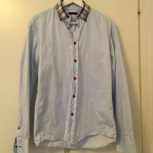 Ljusblå skjorta med fina detaljer: rutig krage och röda knappar, från Jack & Jones. Storlek M