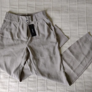 Oanvända! Beige/greige Vero Moda mjuka, högmidjade kostymbyxor, storlek 34 - Oanvända beige högmidjade och bekväma kostymbyxor från Vero Moda. Den första bilden är lånad från hemsidan. 93% viskos och 7% polyester. Storlek 34.