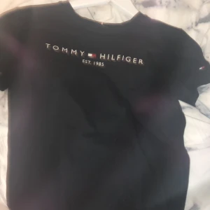 Svart tommyhilfiger t-shirt  - Säljer nu min svarta tommyhilfiger t-shirt då den inte kommer till användning använd ca 5 gånger! Bra skick! Inget fel på den! Skriv för fler bilder eller frågor osv! Den är i storlek 140 kan även passa som 150! Pris kan diskuteras!💕💕