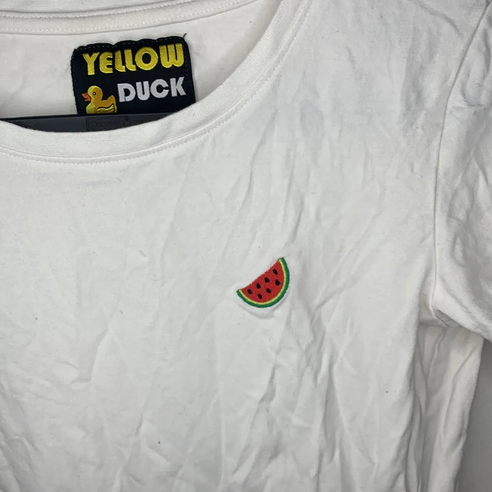 En T-shirt med en söt vattenmelon bit på höger sidan på bröstet. Inga resterande mat eller trådar på plagget.. T-shirts.