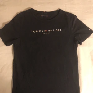 Tommy Hilfiger T-Shirt - En fin marinblå Tommy Hilfiger tröja i mycket bra skick! Nästan oanvänd. Den är i storlek 176 men skulle säga small/medium. Hilfiger märket fortsätter från kragen till lite på baksidan. DMa för fler bilder❤️                                                             NYPRIS: 549kr 