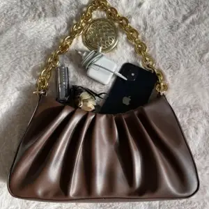 En väska som är brun med guld kedja med samettyg inuti med ett litet fack 