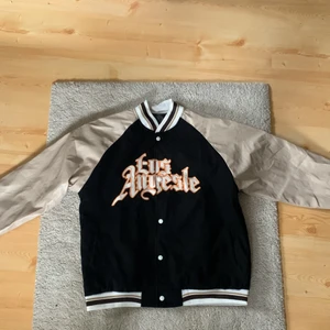 Varsity/college jacka, strorlek M/S - Varsity/college jacka, strorlek L men den passar som storlek M/S. Skicket är nytt då den är oanvänd eftersom den inte passar mig som är 190 cm. Den är svart, beige, brun och orange i färgen.
