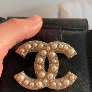 Chanel brooch - Säljer min brooch som är köpt från Chanel i Stockholm. Den är guldfärgad med pärlor och strass. Broochen är i nyskick och kvitto, ask samt tillhörande chanelpåse medföljer. Priset är inte förhandlingsbart.