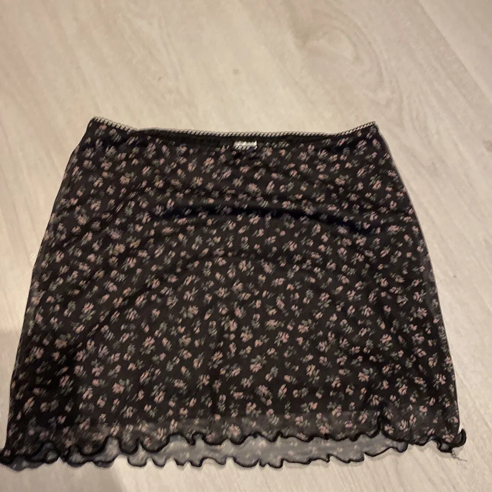 En svart blommig mini skirt i storlek xxs oanvänd (köparen står för frakt). Kjolar.