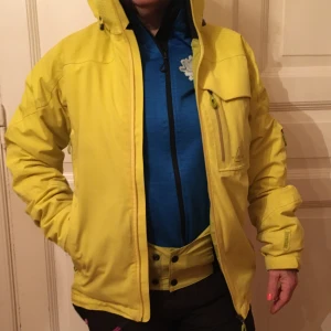 Skidjacka SOS storl S - Gul skidjacka med massor av bra funktioner, snölås, avtagbar huva, går att öppna i ärmhålen, ficka för liftkort… av märket SOS, Sportswear of Sweden. Mycket bra kvalitet och i mycket gott skick. Syns i backen! 
