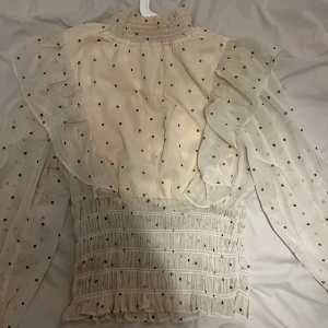 NA-KD blus i storlek 36 - Säljer min blus från nakd i storlek 36. Den är vit/beige med bruna prickar och blusen har en volang resår nere som formar sig efter midjan, kragen är lite högre och ärmarna är jättefina🤍