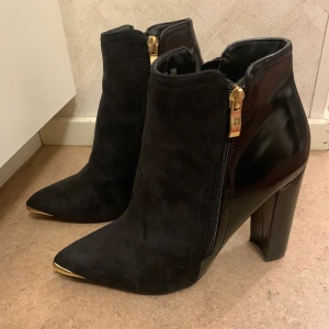 Svarta ankelboots med klack stl 38 - Svarta vinterklackskor med gulddetaljer och olika tyger, ett som är mer glansigt och ett mockatyg (jämf. Bild). Använda endast en gång och i gott skick.   Klackhöjd ca 8cm Jag kan mötas upp i Stockholm men även skicka skorna, dock står du för frakten.