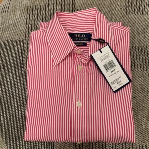 Polo Ralph Lauren skjorta - En helt ny Polo Ralph Lauren skjorta jag fick i present som är för liten. Storlek XS röd och vit randig. Bra skick, inga lösa trådar. Tjejmodell går in vid midjan lite. Nypris 1200kr