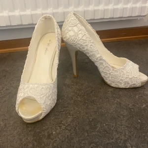 Klackskor  - Klackskor i färgen vit + spets. Skorna är använda en gång men aldrig efter det. Är i bra skick. 