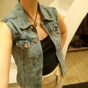 Ljus jeansväst - Ljus jeansväst med kopparfärgade knappar och två bröstfickor. 