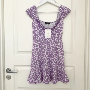 Blommig Klänning - Lila blommig klänning från Bershka vita blommor  Helt ny med prislapp  Storlek XS  Nyskick Jättefin till våren & sommaren 💞