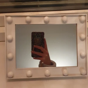 Spegel med lampor - Den har stått på en hylla och inte har varit så mycket använd. En liten prick som är lite svår att få bort.Går på batterier! 14 lampor.