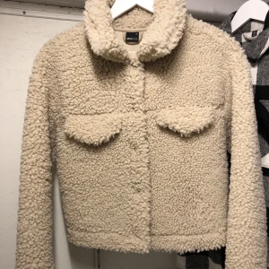 Croppad beige jacka i teddymaterial - Croppad jacka i teddymaterial, från Gina tricot i storlek xs, använd fåtal gånger så i jättebra skick! Kan skicka fler bilder vid önskemål. 
