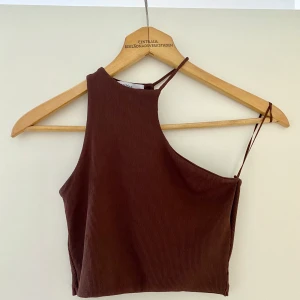 Topp  - Mörkbrun topp med en arm och detalj vid halsen från Bershka i storlek XS.