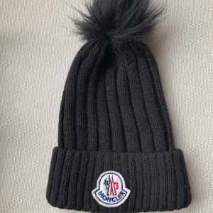 Mössa Moncler - Mössa med pälsboll på topp. I fint skick och verkar sparsamt använd. Har trott att den varit äkta men är tveksam då den saknar care-tags, om de inte blivit borttagna. Fin iaf. 