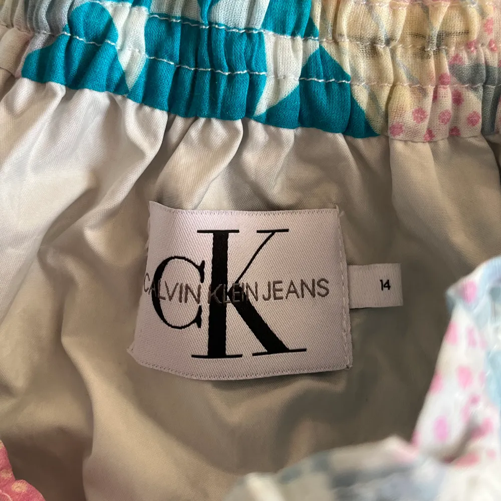 Färgglad och väldigt häftig kjol från Calvin Klein! Två lager tyg där det understa är silver och översta är en blandning av färger och CK loggan. Inte använd många gånger, utan i väldigt fint skick! Storleken är 14.. Kjolar.