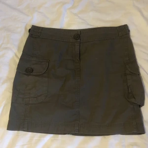 kjol  - Militärgrön kjol med två sidfickor och justerbara knappar vid midjan så att man kan göra mindre eller större runt midjan!