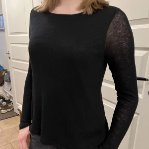 Långärmad stickad topp  - Stickad svart tröja med slitsöppning. Innertröjan av silke liksom rosetterna. Stretchig och stor nog att passa Large. Mycket gott skick. 