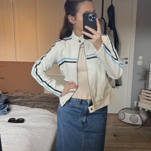 Motojacket - Perfekt vårjacka!!! Vitt PU leather med blå och svarta ränder. Skön, unik och snygg. Köpt second hand i mycket gott skick och aldrig använd av mig. Därför är det hög tid att någon annan får njuta av denna perfekta jackan i vår!!!💘